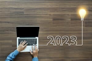 person typing "2023" on laptop. Includes a graphic of a lightbulb (how long should blog posts be)