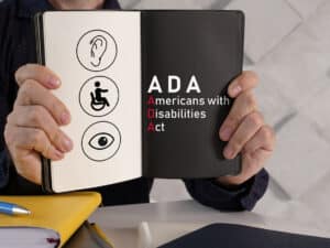 person holding open a book with graphics that says "ADA" and "Americans With Disabilities Act"