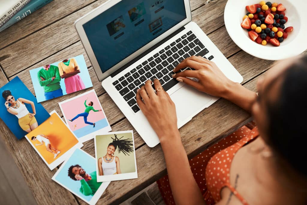 woman typing on a laptop with a bowl of fruit to her right and pictures to her left 